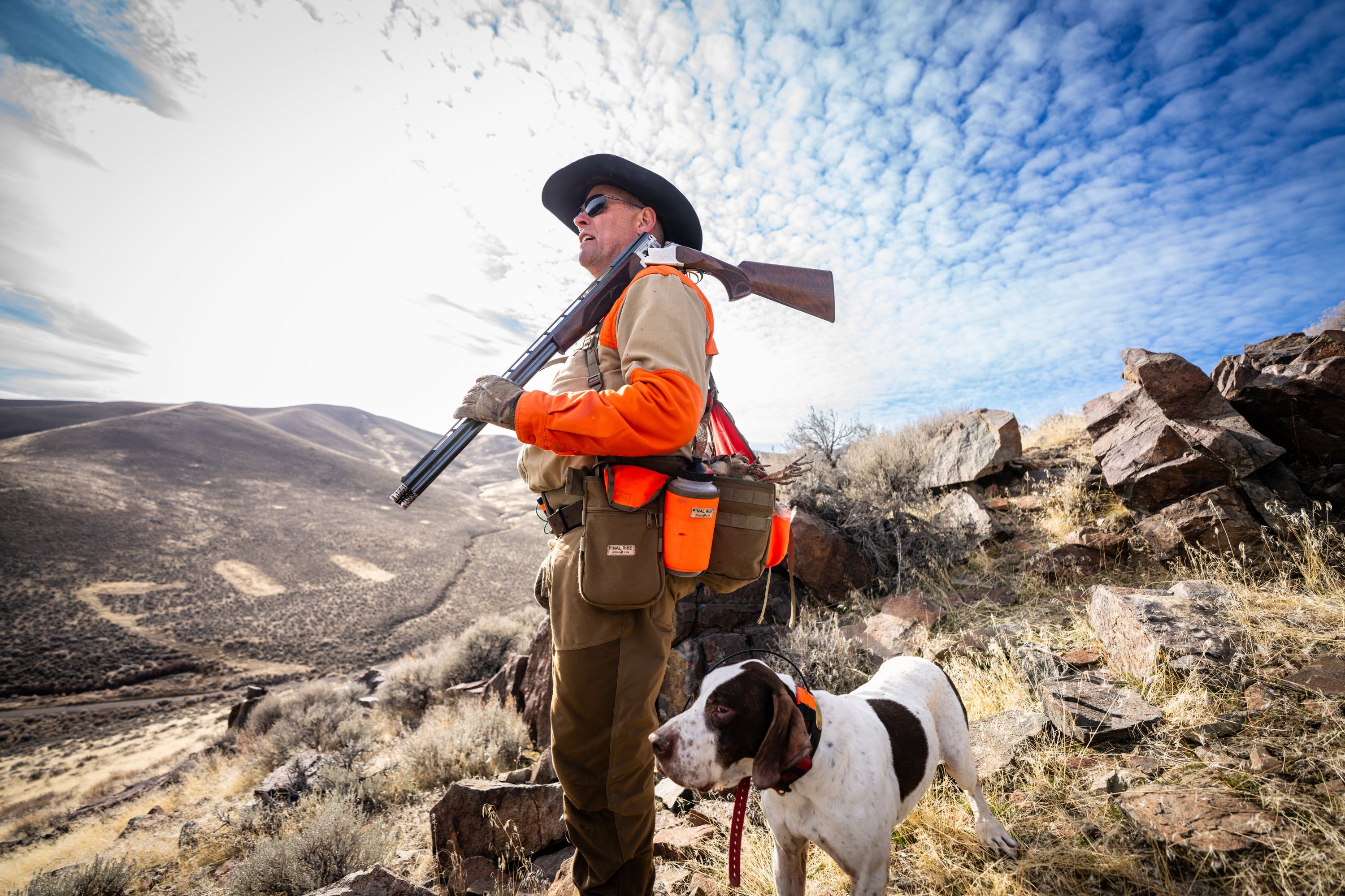 Hunter with a shotgun and dog in a mountain desert landscape